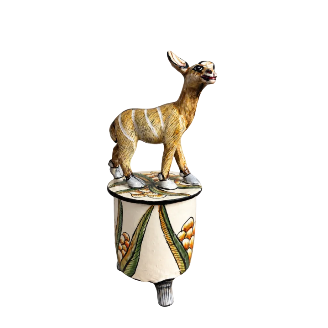 A hand-painted ceramic Dutch deer figurine standing on a patterned cylindrical pedestal, photographed against a neutral light gray background.
