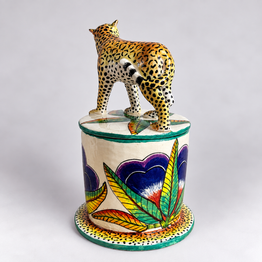 A hand-painted ceramic decorative trinket jar with a painted leopard figurine on top, set against a neutral light gray background.