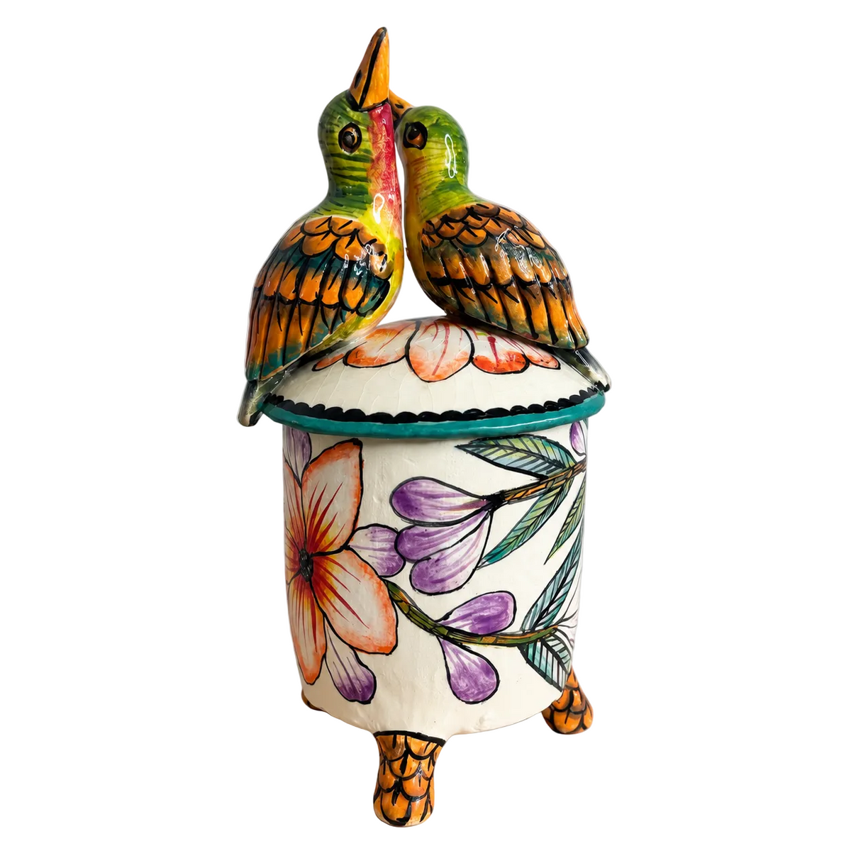 A hand-painted ceramic lidded container with two small colorful birds perched on top. The cylindrical body is cream-colored with purple flowers, green leaves, and orange accents, while the birds add vibrant green, orange, yellow, and pink details.