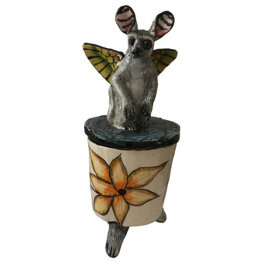 This handcrafted ceramic trinket box features a whimsical bushbaby perched atop the lid, complete with beautifully painted butterfly wings.