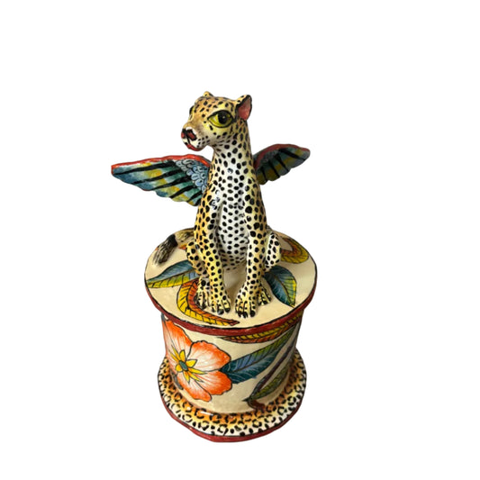 A hand-painted ceramic figurine of a leopard with wings, mounted on a matching cylindrical pedestal decorated with floral and bird motifs, set against a plain white background.