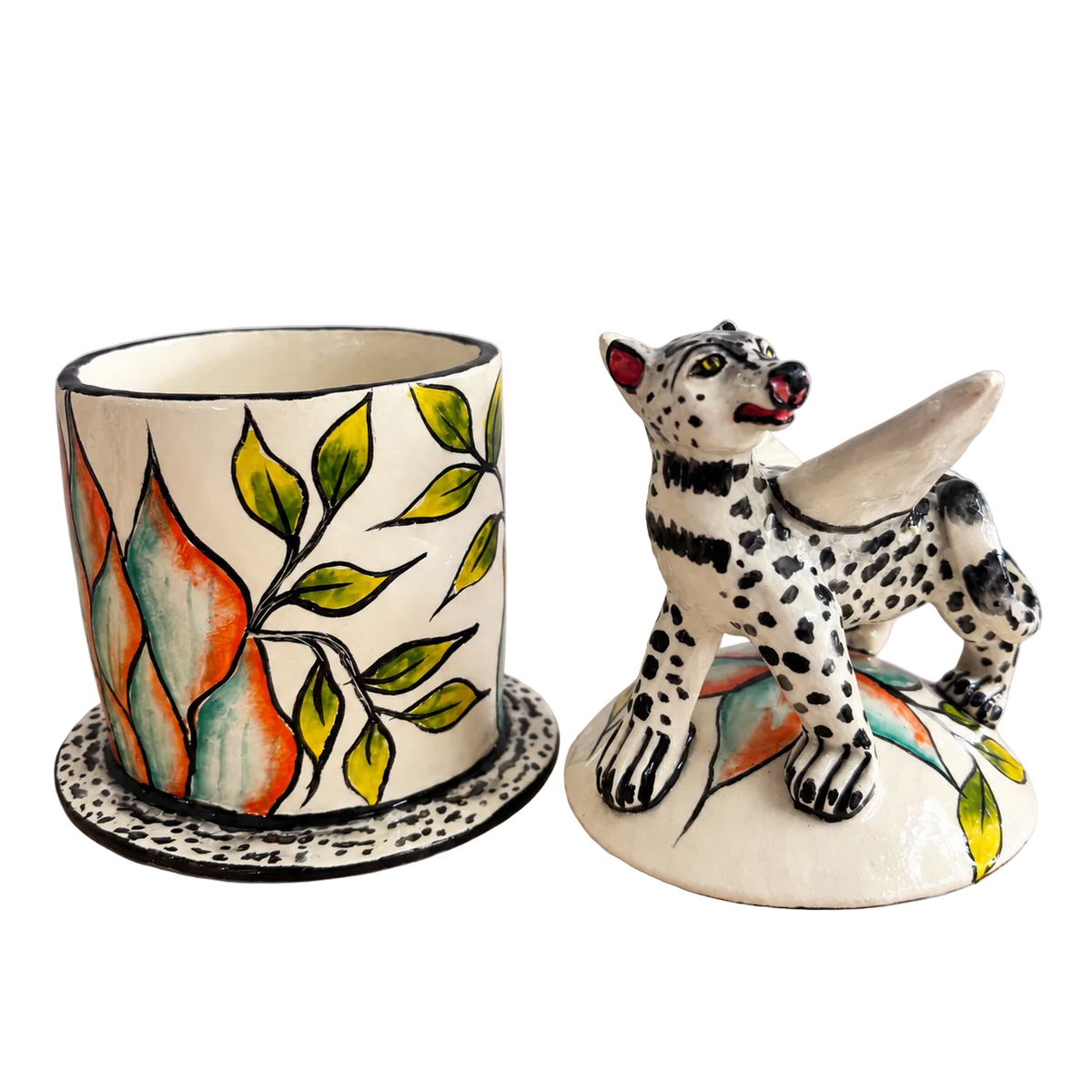 A ceramic jar and matching lid set on a light gray background. The jar has a cream-colored body decorated with a painted green leafy vine and orange-red leaf shapes, sitting on a matching saucer.